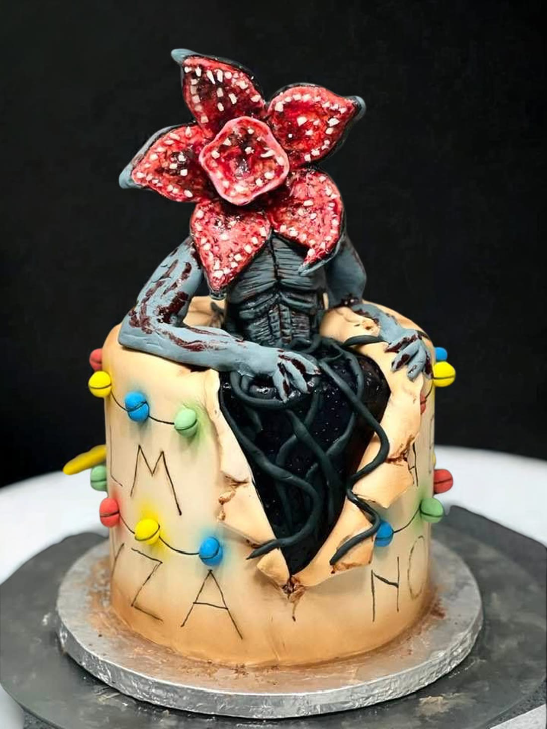 A sculpted creature breaking out through the side of a cake, with fairy lights around it.