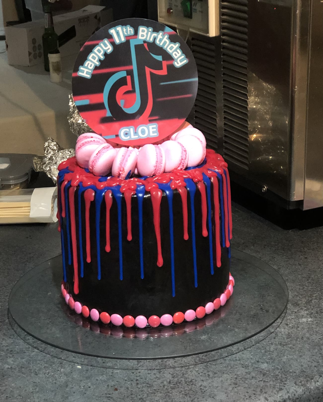 A black cake with red and blue drips, macarons on top.