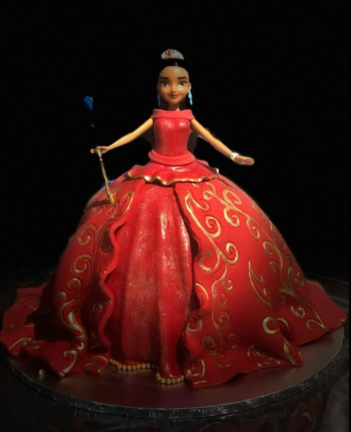 A doll cake with a wide red gown piped in gold scrollwork.