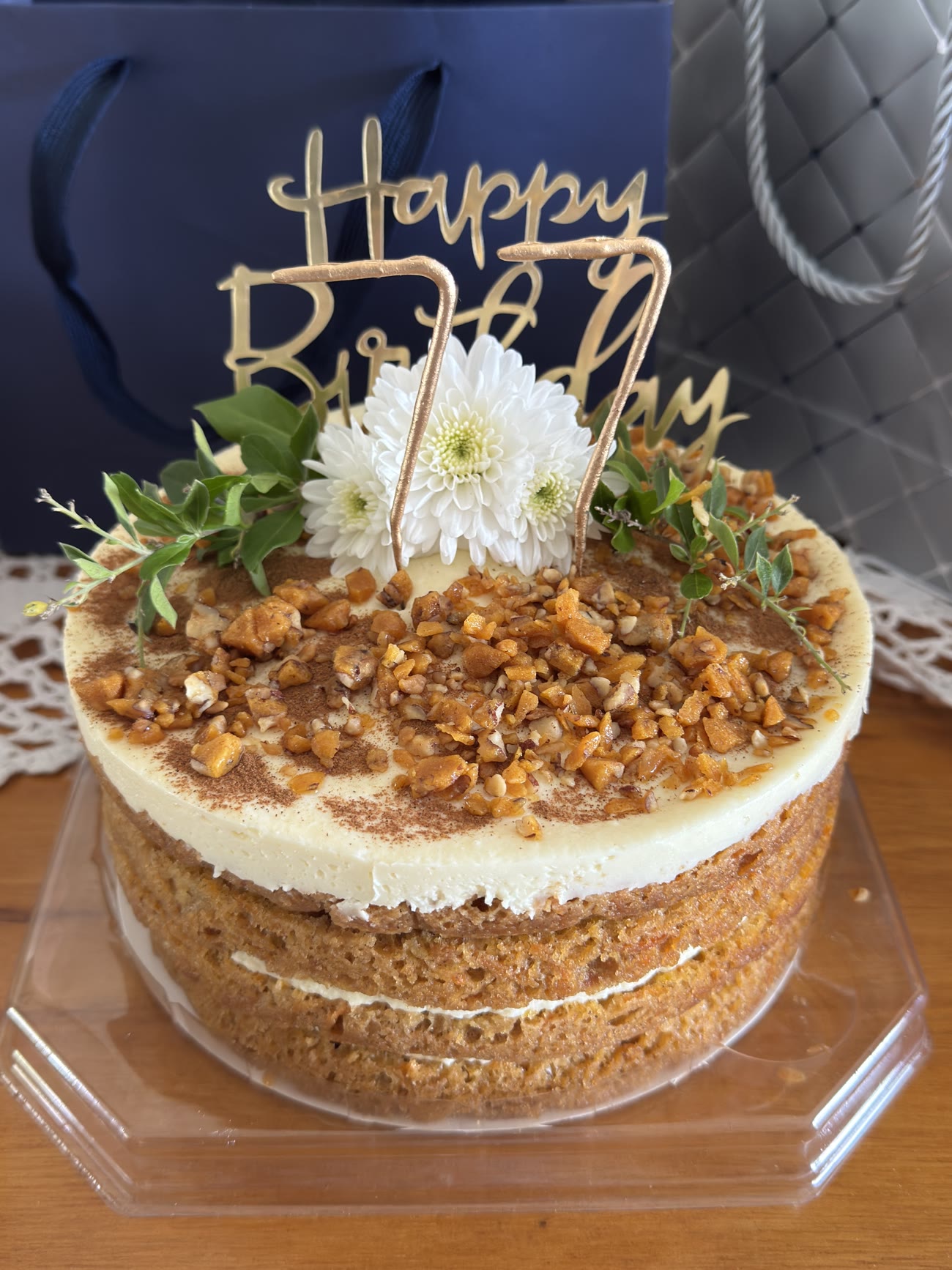 A cake with bare sides, chopped nuts around the top and flowers.