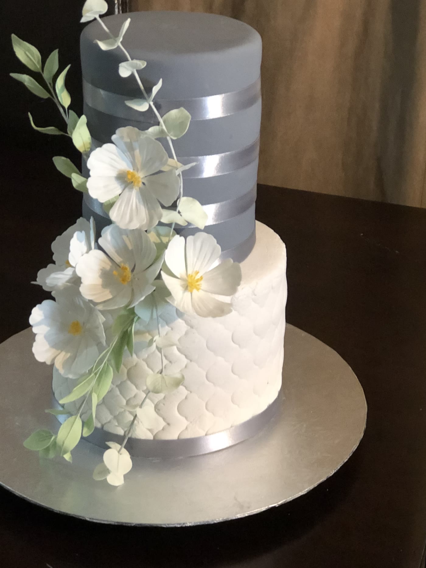 A two tier white and silver cake with sugar flowers.