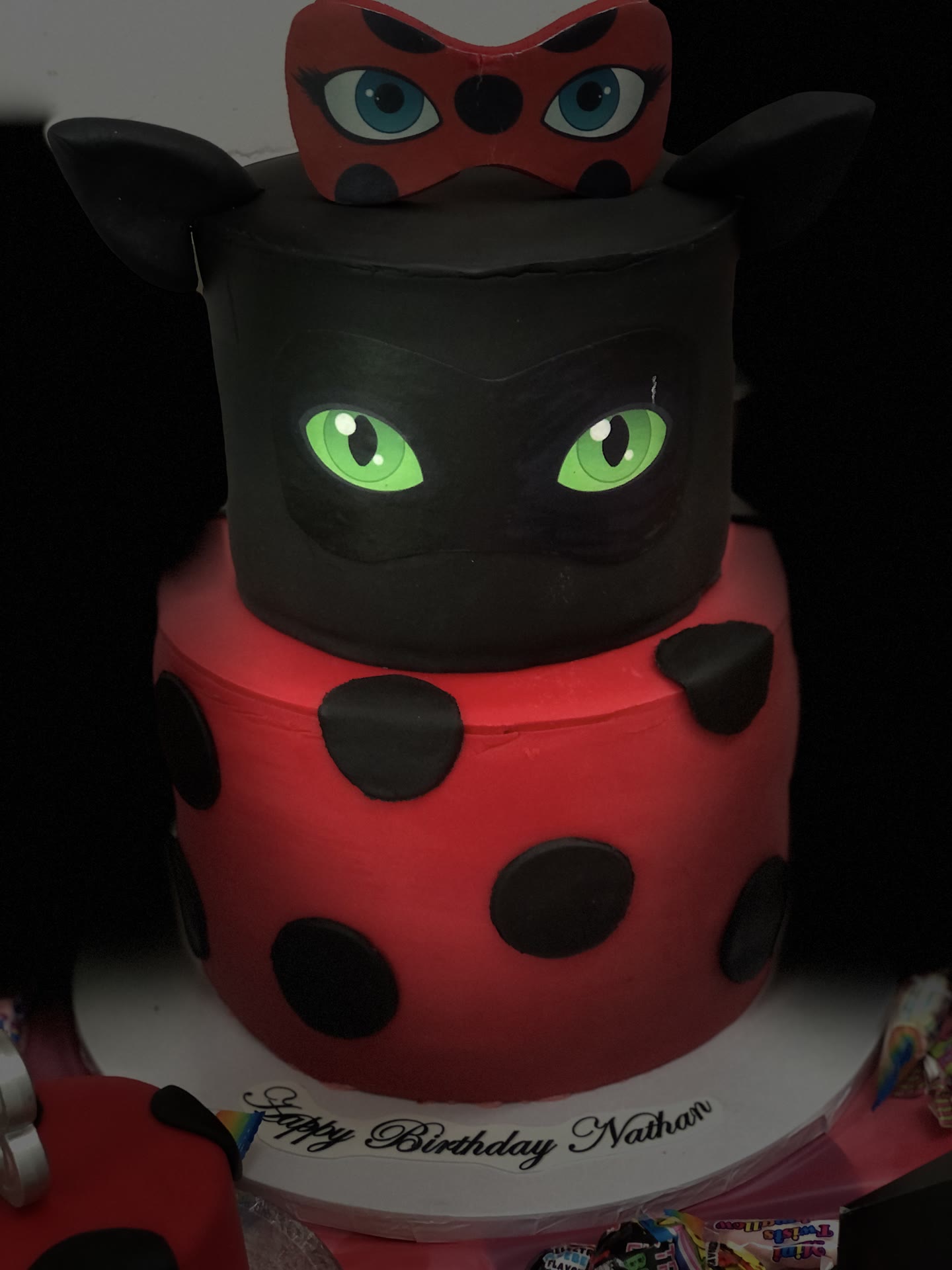 Two tier cake, red spotted base and a black sculpted head with green eyes.