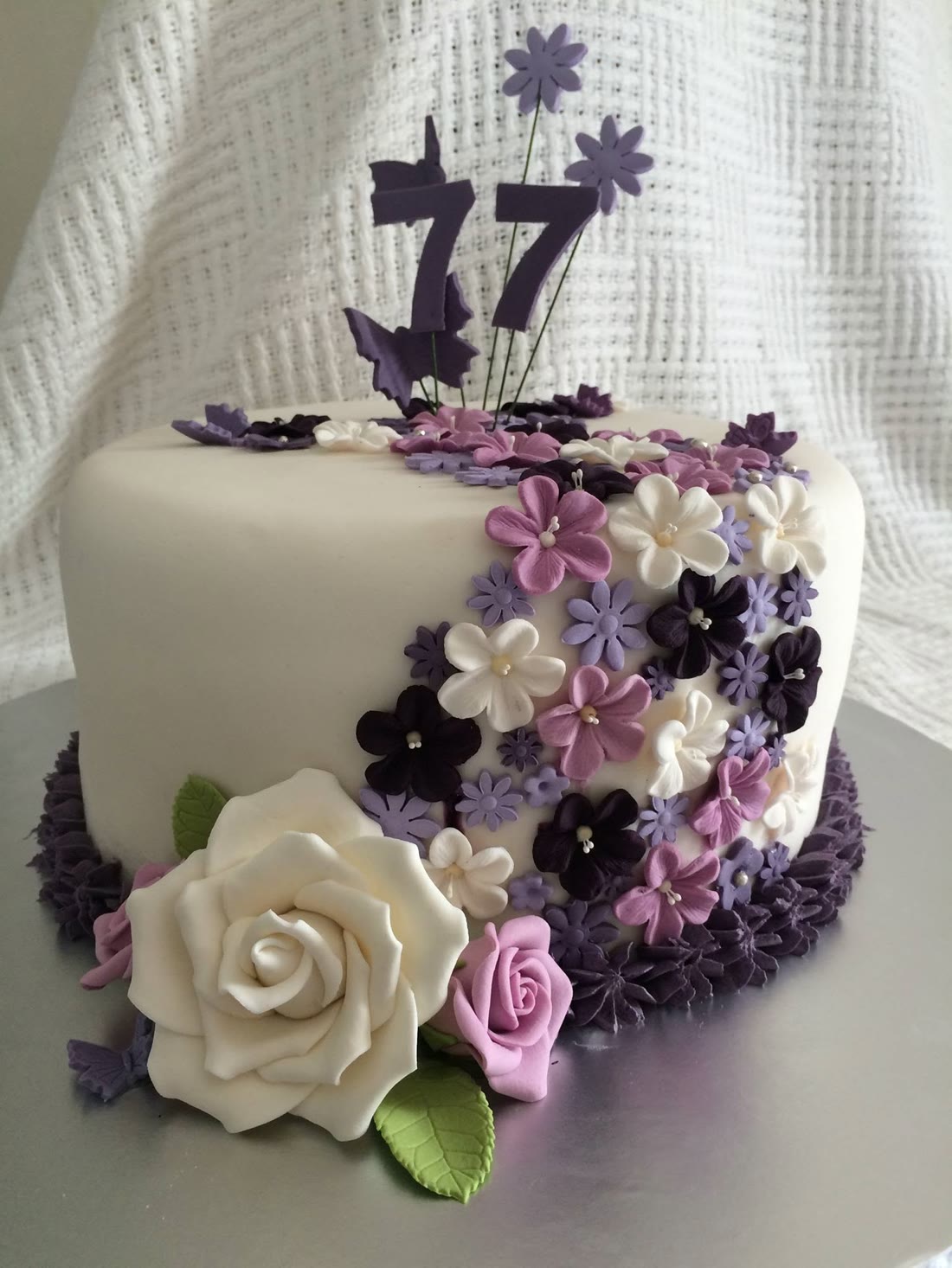 A white cake with a cascade of purple and cream sugar flowers.